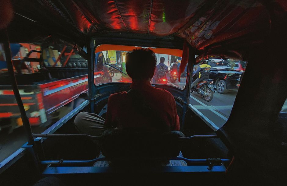 A tuk-tuk driving through a bustling street in Phnom Penh, Cambodia, with local architecture in the background