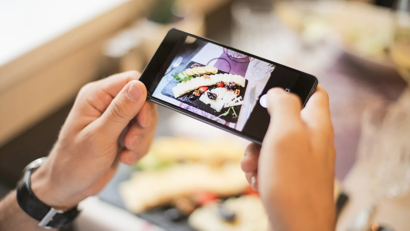 Hands photographing a plated dish on a restaurant table with a smartphone