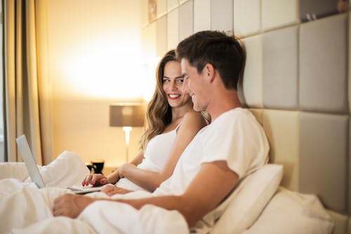 Free Smiling young couple browsing laptop together on bed Stock Photo