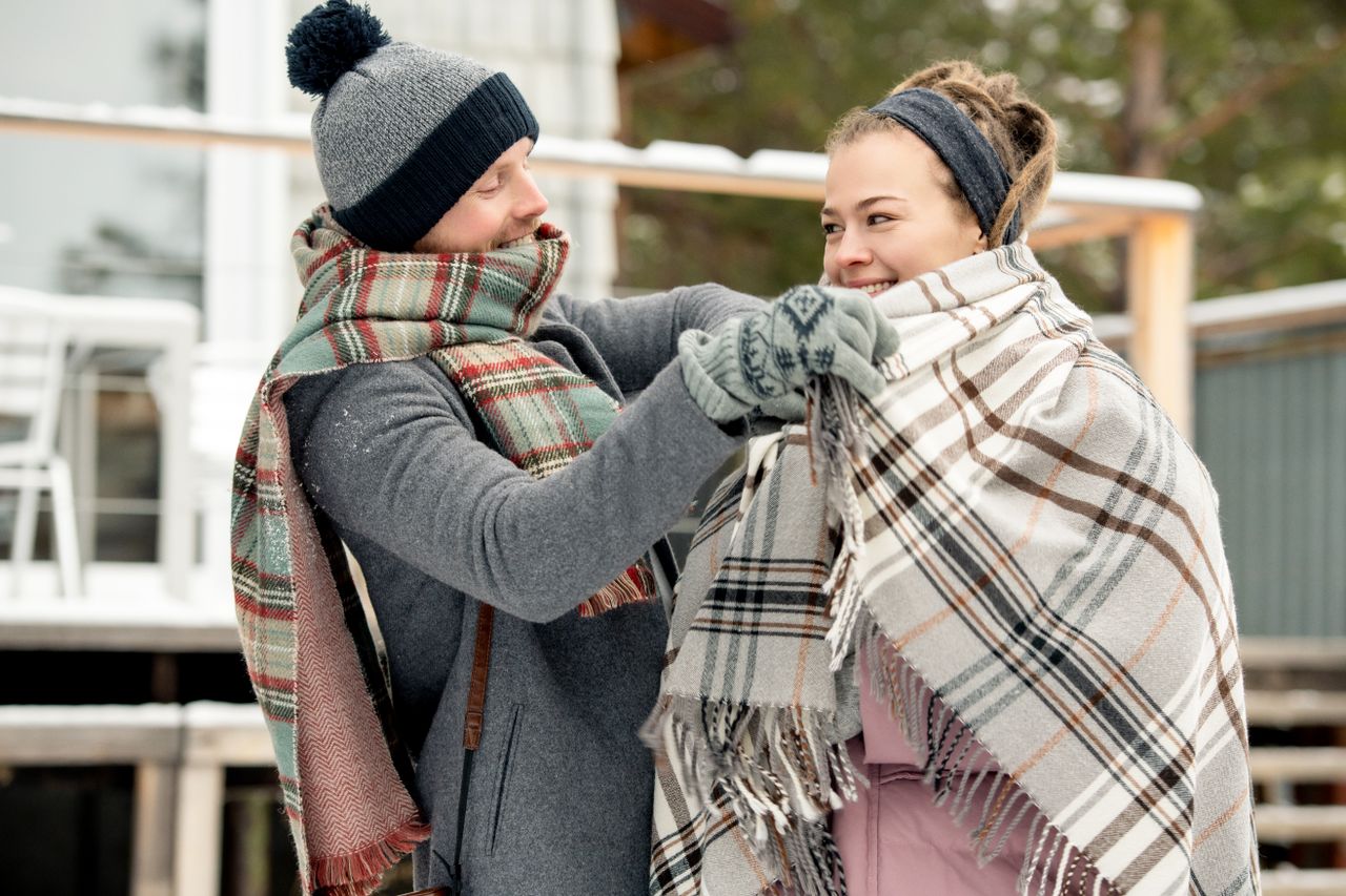 Two women in plaid scarves, one adjusting the other's scarf outdoors
