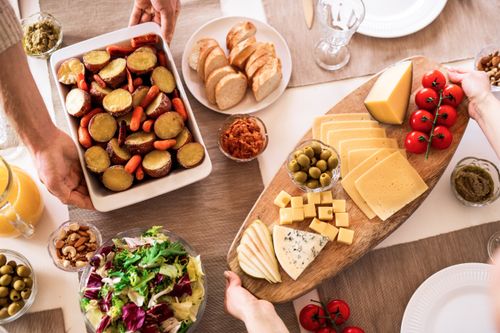 Free Delicious cheese platter with fresh vegetables, olives, and bread on a dining table. Stock Photo