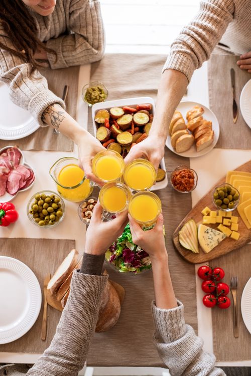 Free Top view of friends toasting with orange juice during breakfast with a variety of foods. Stock Photo