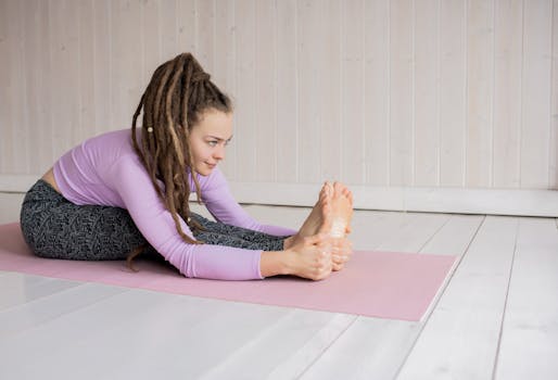 Woman practicing yoga indoors, performing forward bend on a pink mat in a serene setting.