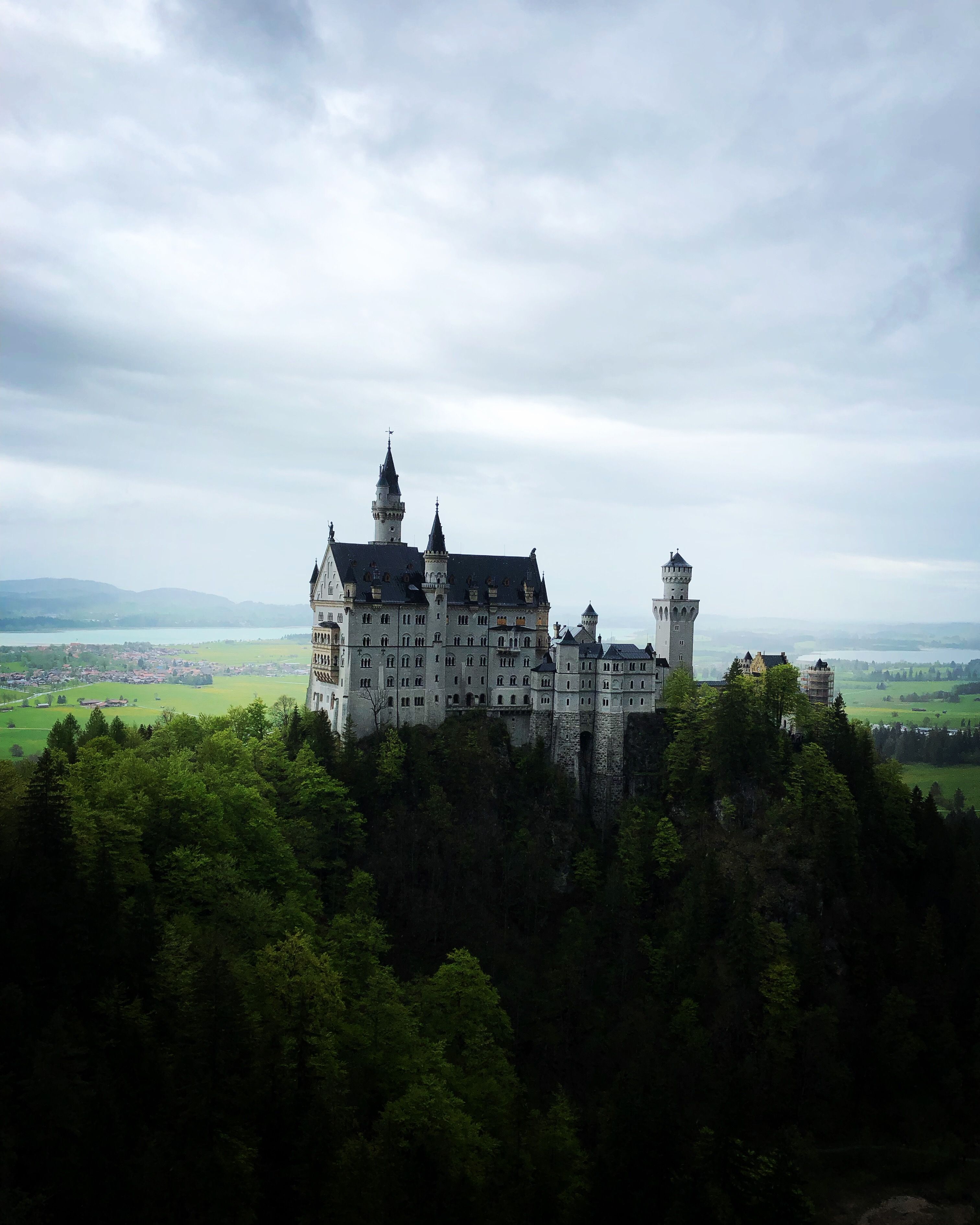 Stunning aerial view of Neuschwanstein Castle surrounded by lush greenery and mountainous backdrop in Schwangau, Germany.