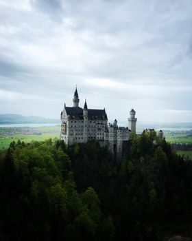 Stunning aerial view of Neuschwanstein Castle surrounded by lush greenery and mountainous backdrop in Schwangau, Germany.