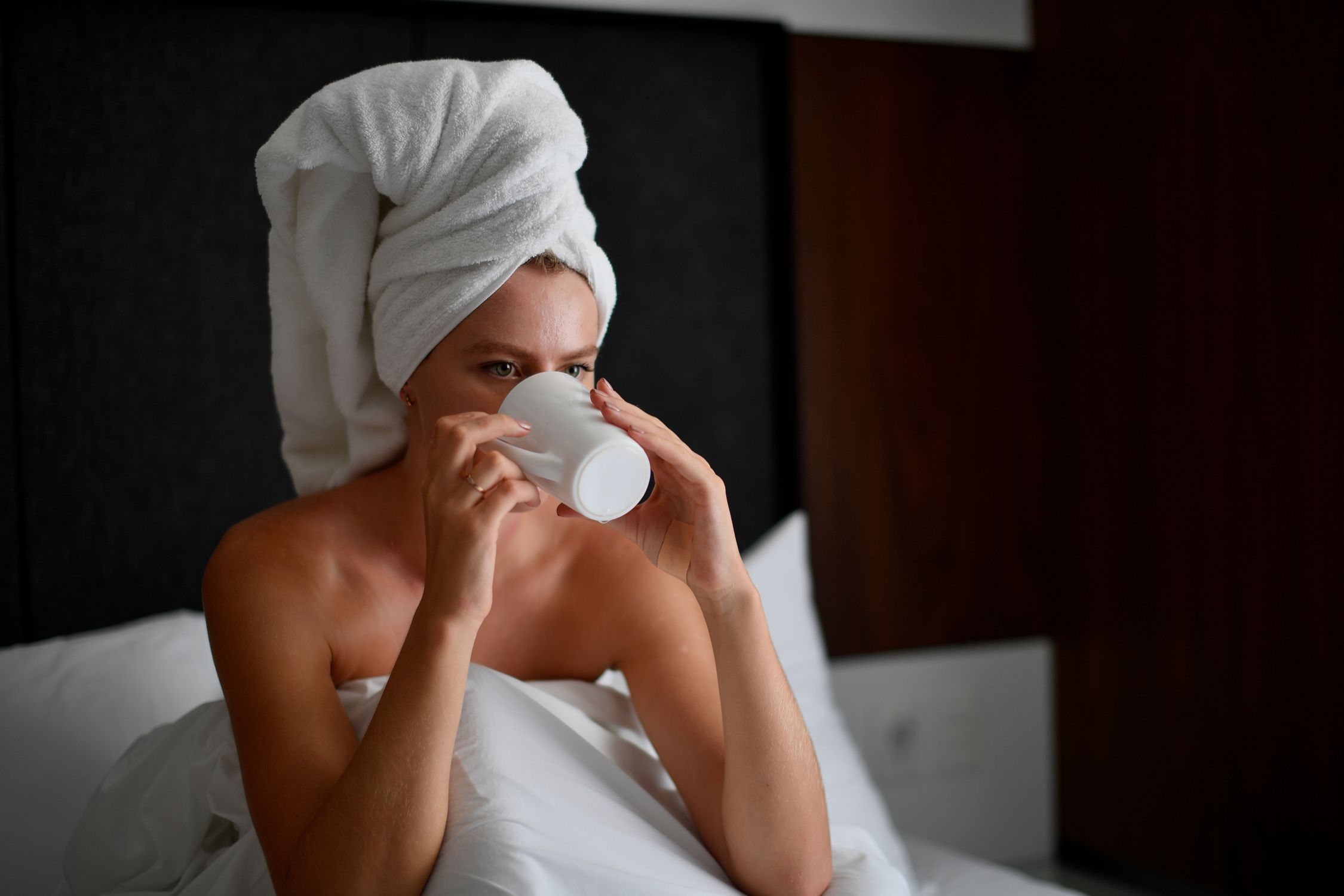 Woman in a towel enjoying a peaceful morning drink in a cozy Cancún hotel room.