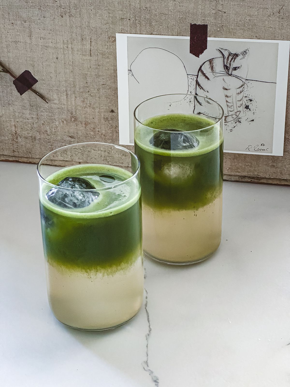 Two iced green and pale citrus drinks in clear glasses on a marble surface