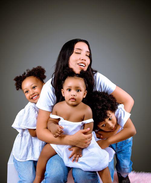 Free A heartwarming portrait of a joyful mother embracing her three children in a studio setting. Stock Photo