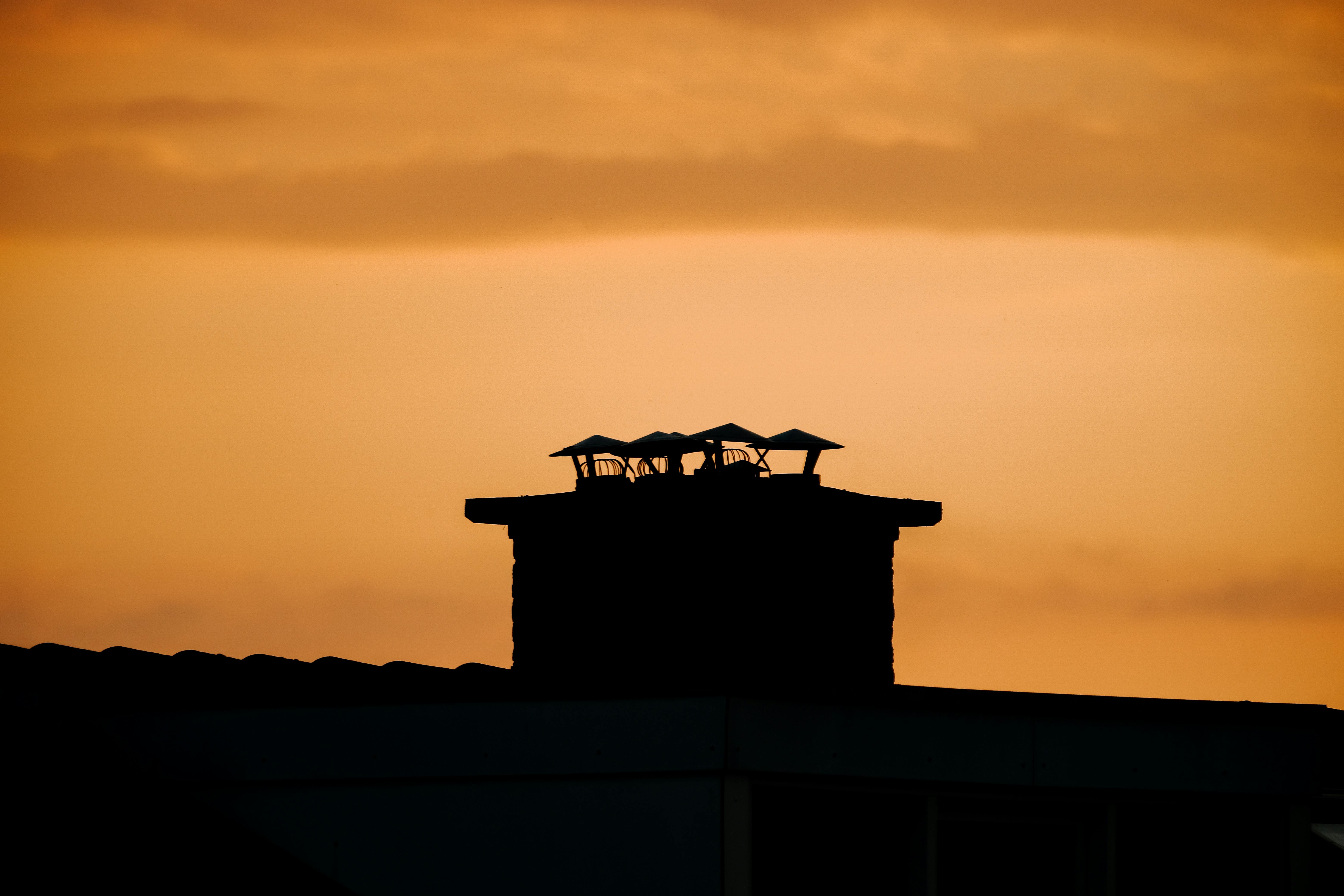 Une cheminée se détachant sur un coucher de soleil orangé flamboyant, offrant un spectacle saisissant dans le ciel du soir.
