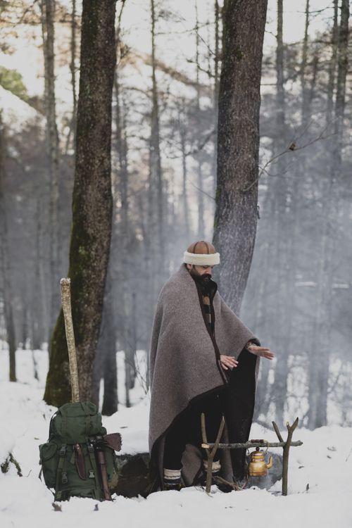 Free A man in winter attire camping in a snowy forest, warming by a fire. Stock Photo