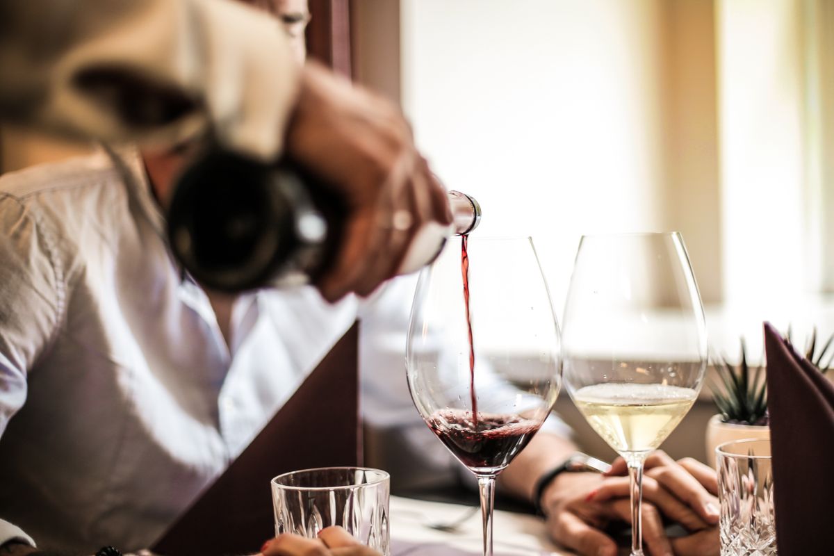 Restaurant server pouring red wine into a glass beside a glass of white wine during dinner service