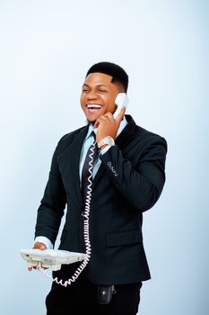 Smiling businessman in a suit enjoying a phone call on a vintage landline, exuding positive energy.