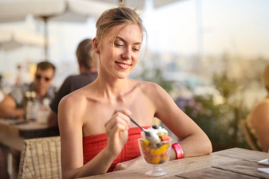 Smiling woman relishes a delicious dessert in a relaxed outdoor cafe setting.