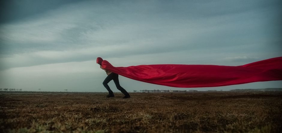 A person in a red cape against a dramatic cloudy sky, symbolizing freedom and movement.