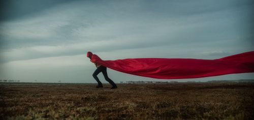 Free A person in a red cape against a dramatic cloudy sky, symbolizing freedom and movement. Stock Photo