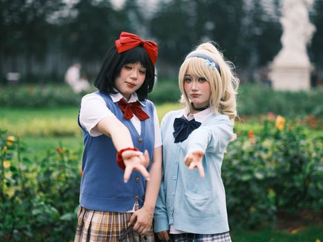 Two adults in anime cosplay outfits posing outdoors in a garden area.