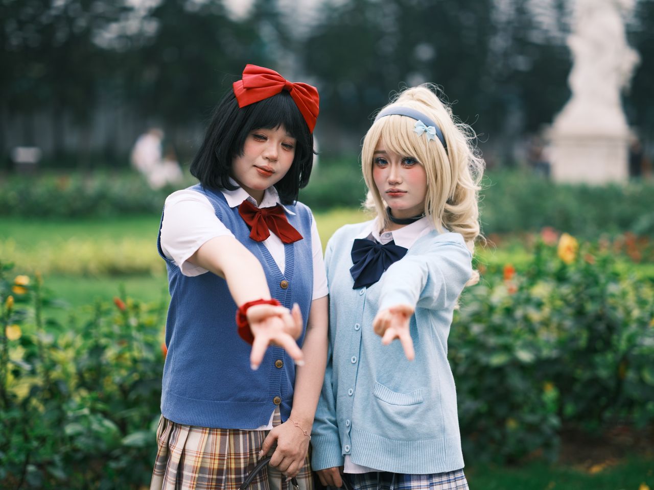 two adults in anime cosplay outfits posing outdoors in a garden area