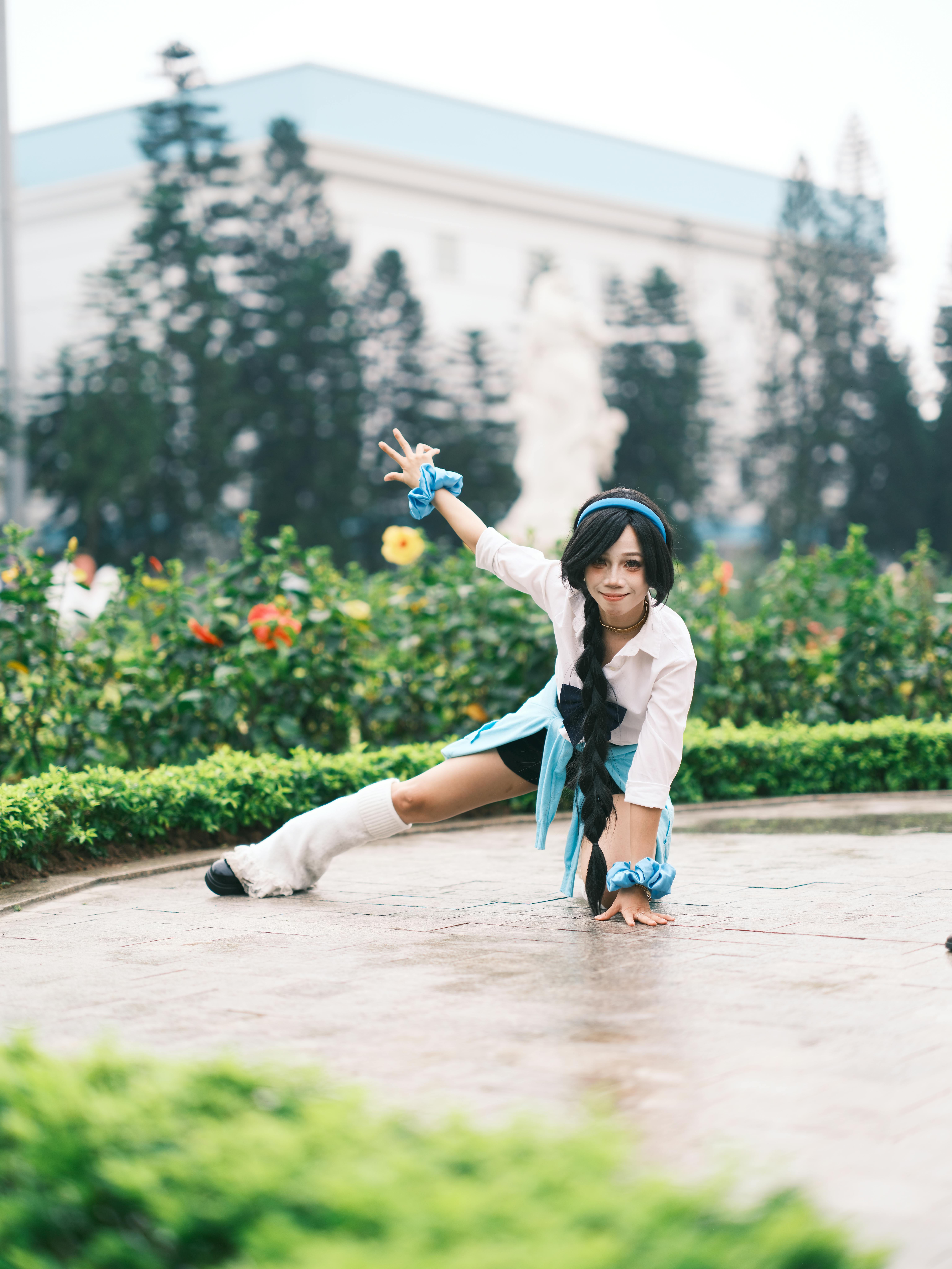 A cosplayer energetically poses outdoors in a colorful garden with costume and props.