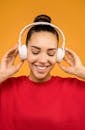 一位穿着红色衬衫、面带微笑的女人，在橙色背景下戴着耳机听音乐