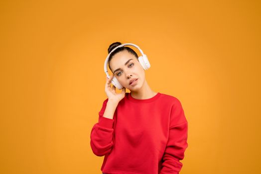 年轻女子戴着无线耳机，在亮橙色的背景中享受音乐