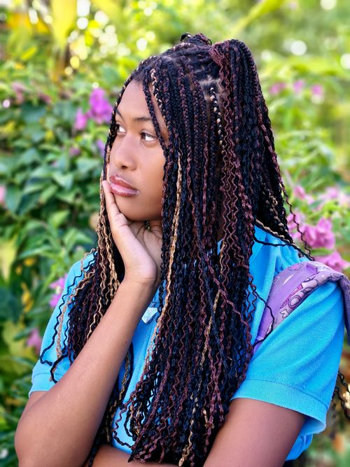 Free A young woman with braids stands thoughtfully among vibrant garden flowers. Stock Photo