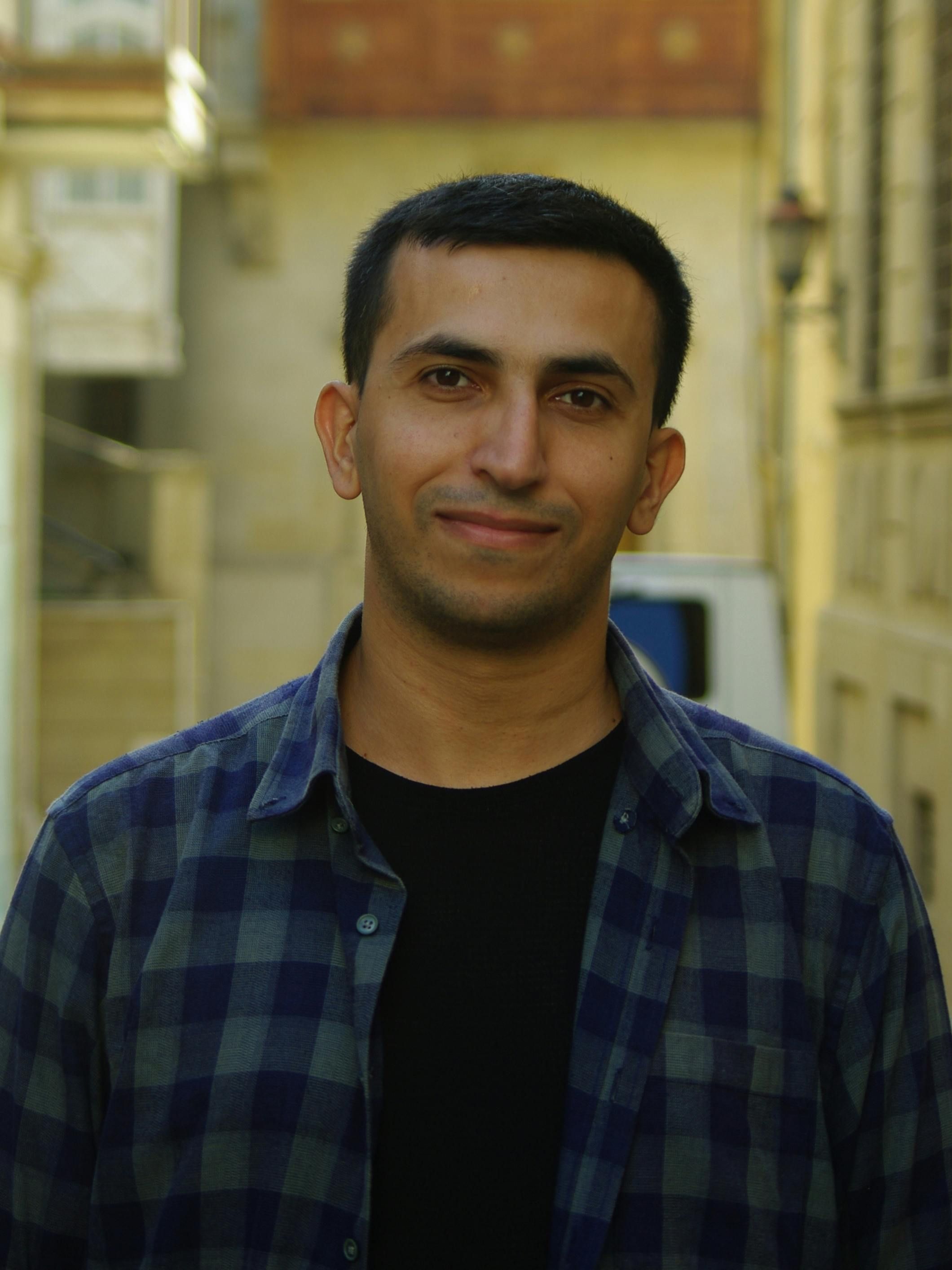 Casual portrait of a smiling man outdoors with blurred urban background.
