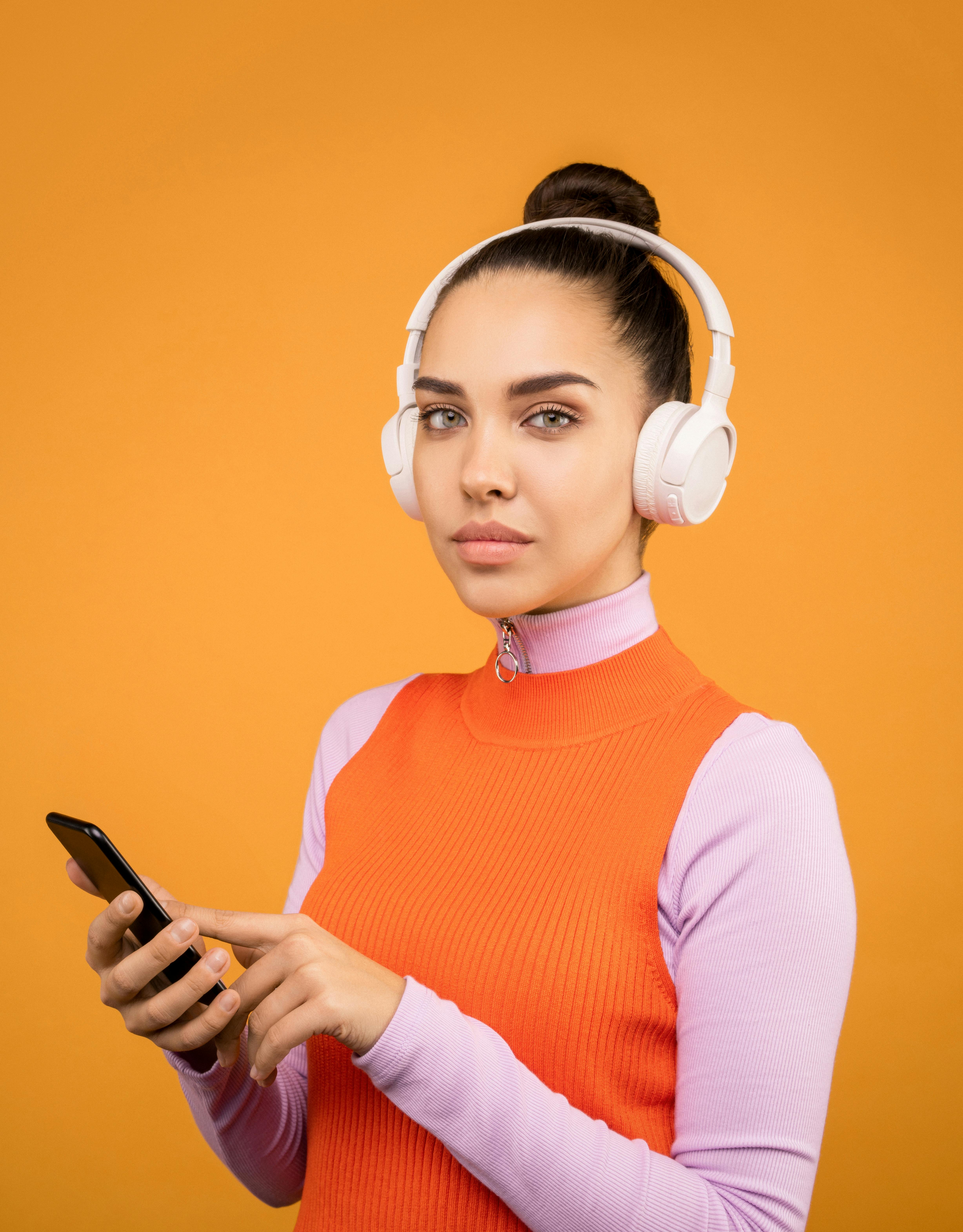 woman in orange and pink turtle neck shirt holding black smartphone