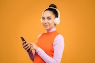 一位年轻女子的肖像，她戴着耳机和智能手机，背景是充满活力的橙色