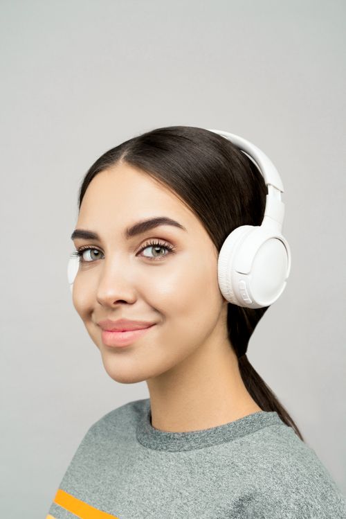 Free Portrait of a smiling young woman wearing headphones, enjoying music indoors. Stock Photo