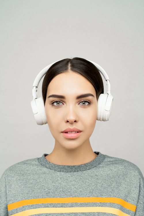 Free Portrait of a young woman wearing headphones, expressing confidence and style in a studio setting. Stock Photo
