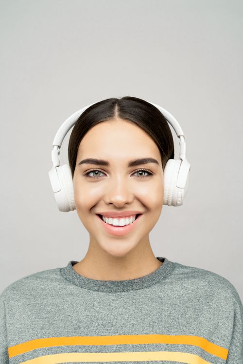 Free Portrait of a young woman smiling and wearing headphones against a gray background. Stock Photo