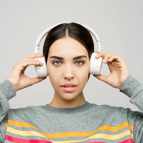 Free Woman in Gray Sweater Holding White Headphones Stock Photo