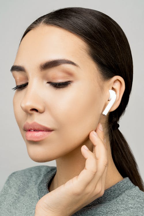 Free Elegant woman with sleek hair wearing wireless earphones, eyes closed in serene expression. Stock Photo