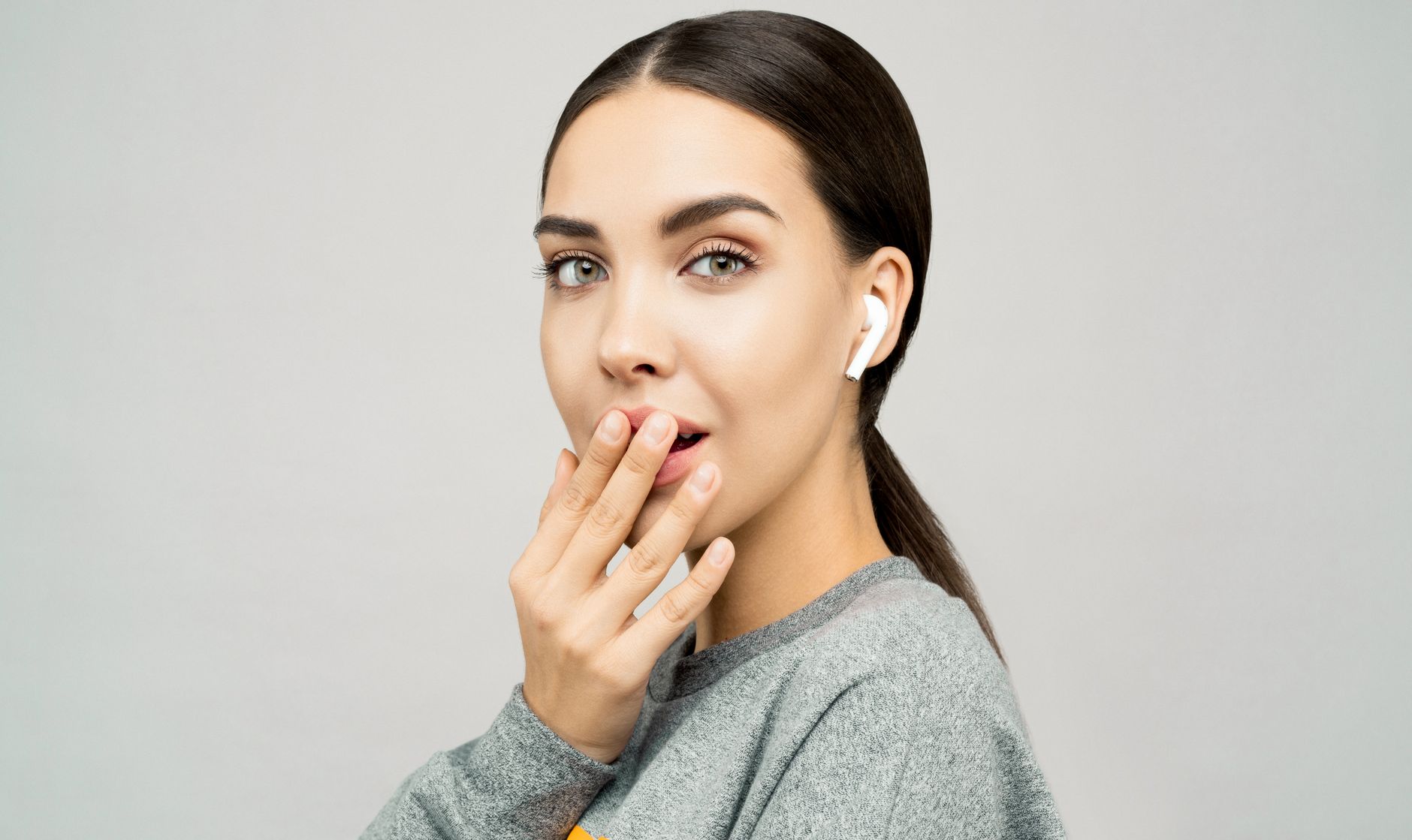 Young woman with sleek hair wearing wireless earbuds and a grey sweater, showcasing a stylish and modern look. Young woman with sleek hair wearing wireless earbuds and a grey sweater, showcasing a stylish and modern look.