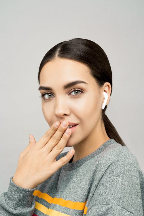 Free Close-up of a smiling woman wearing wireless earbuds, with a playful expression. Stock Photo