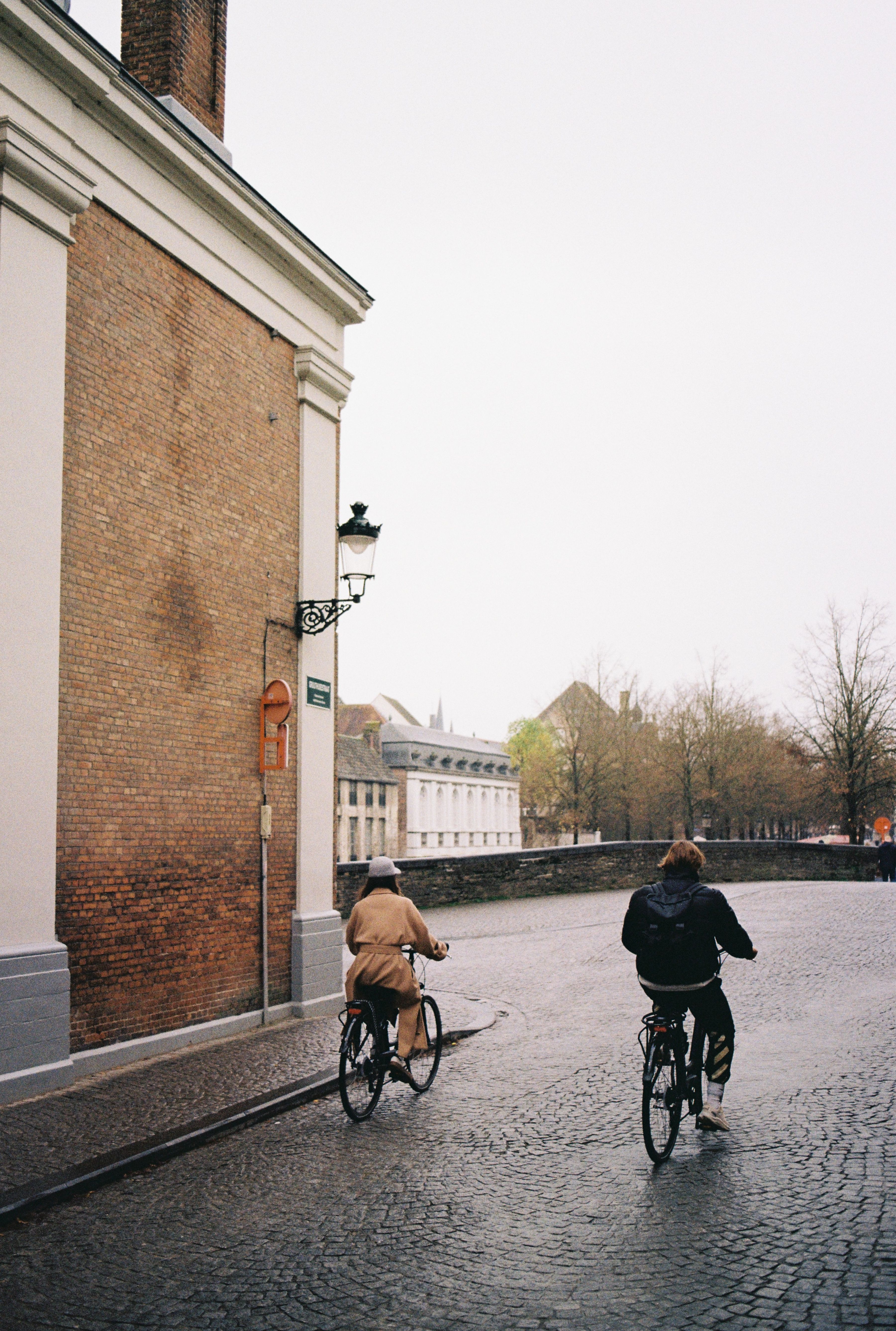 Two people cycling on a cobblestone street near an old brick building, showcasing urban lifestyle.