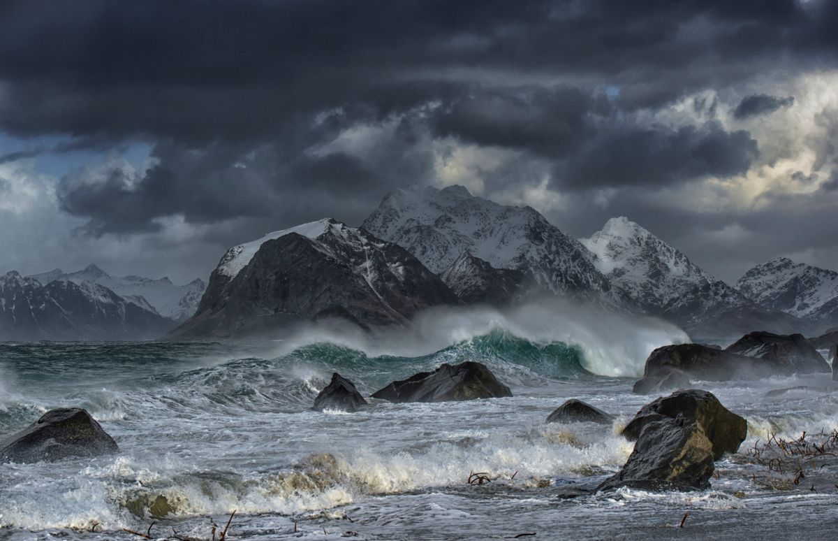 Stormy seas crash against snowy mountains in Nordland, Norway. Captivating and wild.