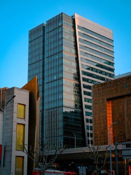 Tall glass skyscraper with urban architecture reflecting sunset light.