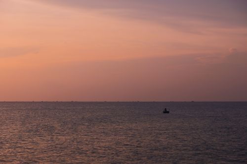 Free A tranquil sunset view over the sea at Phu Quoc Island, Vietnam, with a lone boat silhouette. Stock Photo