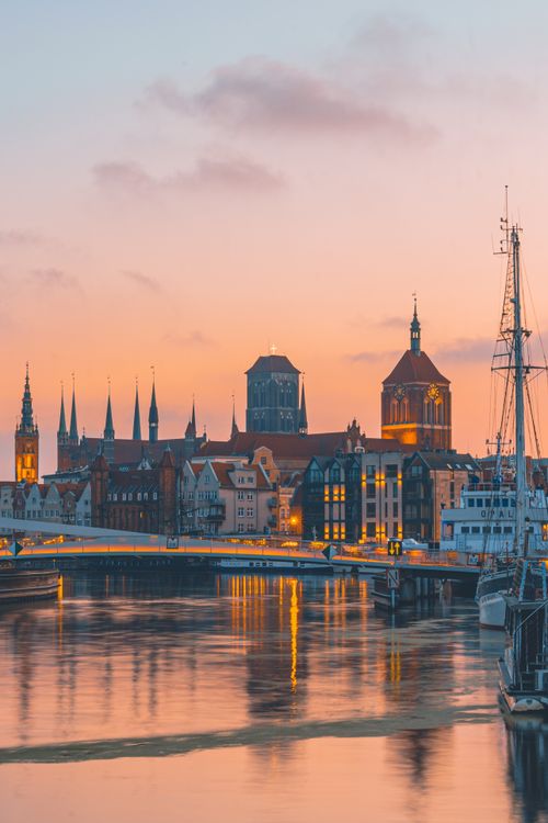 Free Serene view of Gdańsk, Poland's historic skyline reflecting in the Motława River during sunset. Stock Photo