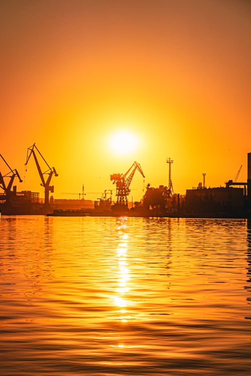 Free Silhouetted cranes at Gdańsk Shipyard capture a breathtaking sunset over the water. Stock Photo