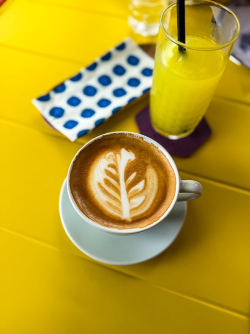 Free Artistic latte with a refreshing drink on a vibrant yellow table setting. Stock Photo