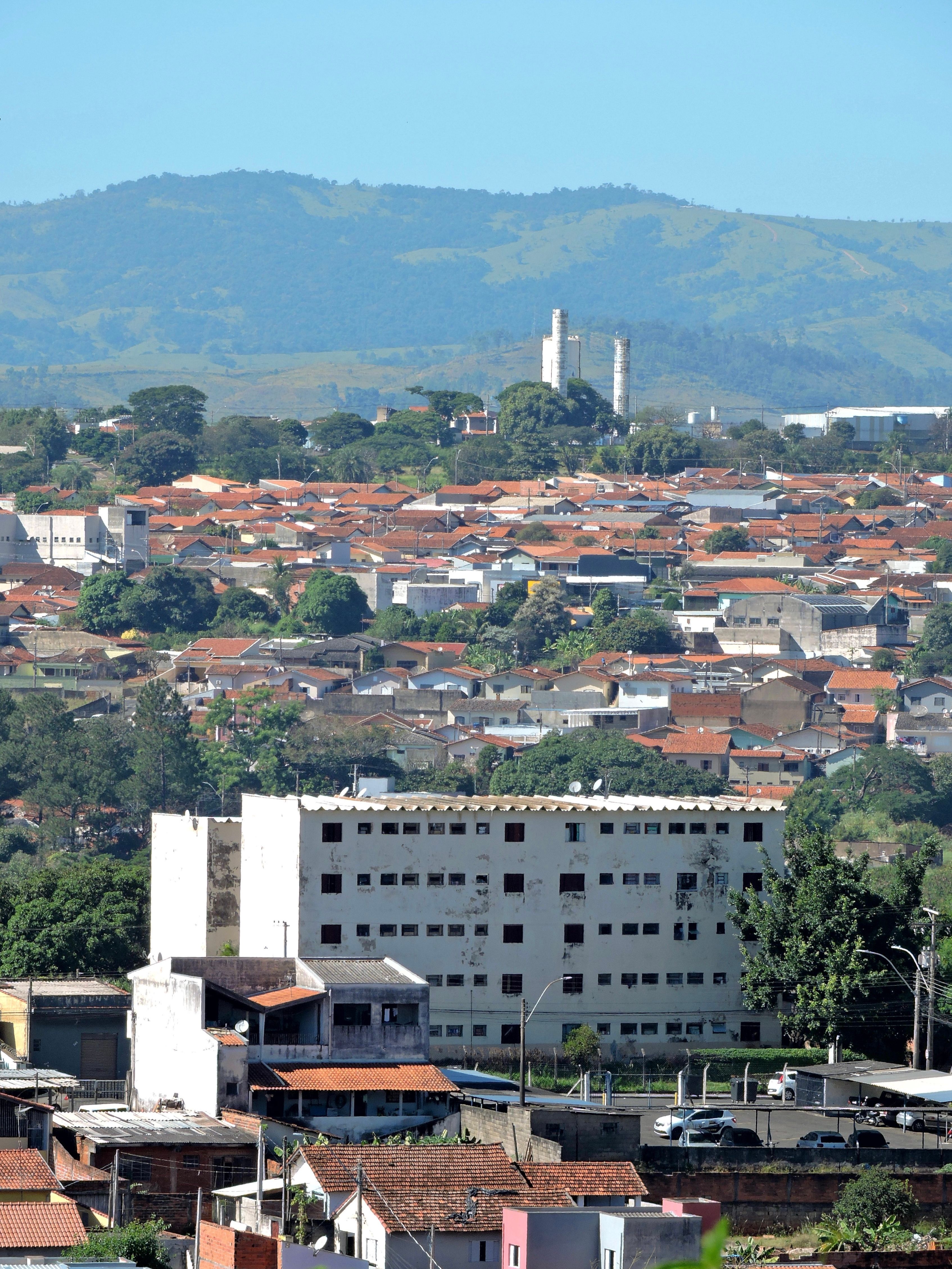 Aerial view of a city with red roofs and a mountainous backdrop under a clear sky.