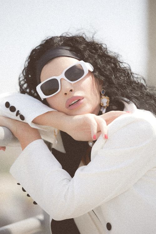 Free Stylish woman in white blazer and sunglasses, posing with elegance outdoors. Stock Photo
