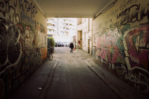 Free Graffiti-covered alleyway in Berlin with a lone pedestrian. Vibrant street art and urban atmosphere. Stock Photo
