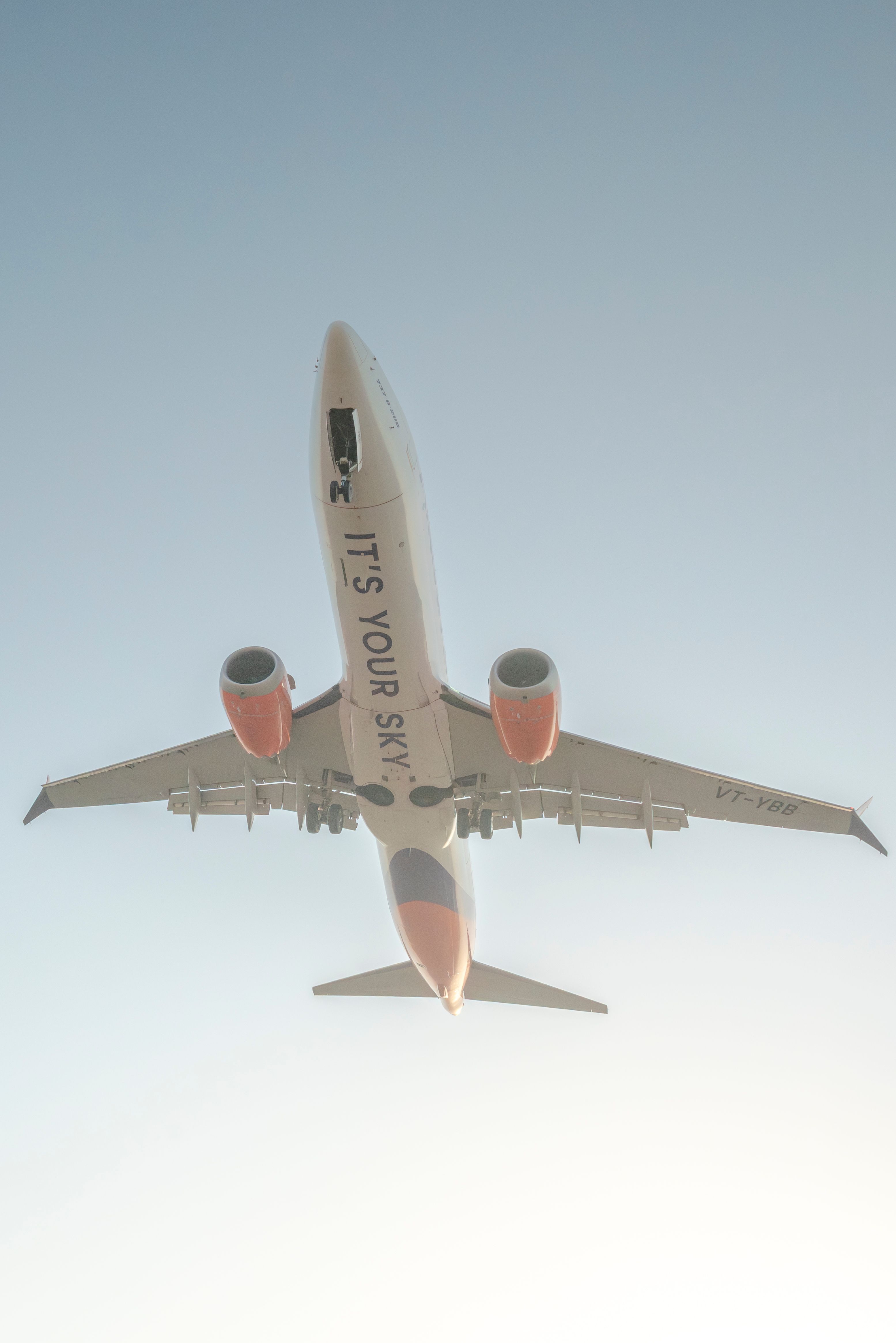 Low-angle view of a passenger jet flying overhead against a bright sky, showcasing modern aviation.