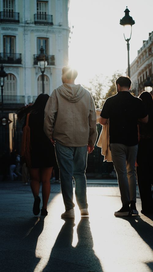 Free People walking in a sunlit urban street, silhouettes against the setting sun. Stock Photo