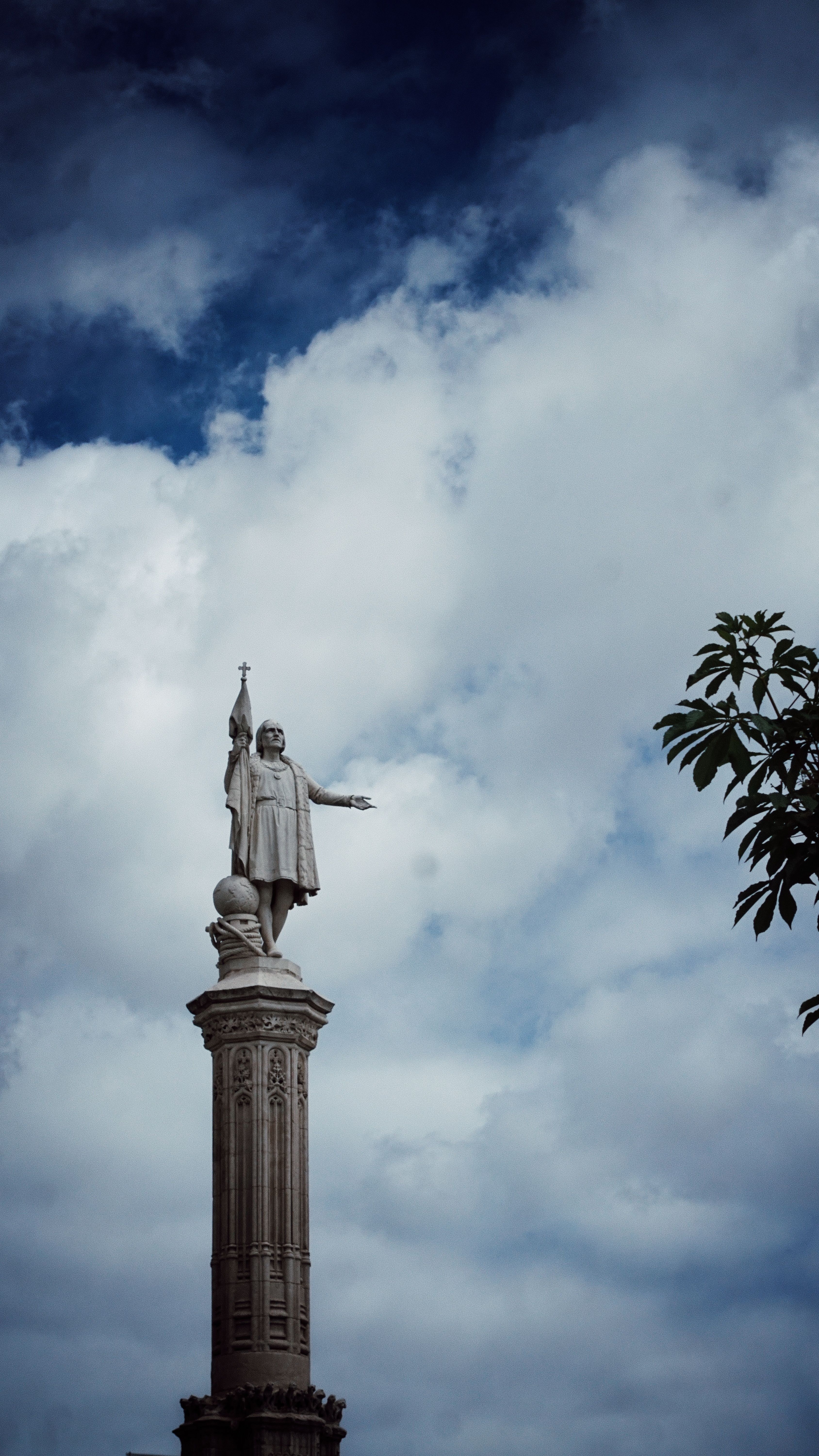 A statue on a column set against a dramatic and cloudy sky, evoking grandeur.