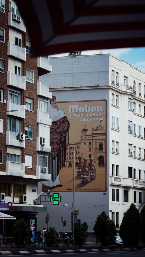 Free Urban scene with Mahou beer mural on Madrid street. Captures local architecture and vibrant street life. Stock Photo