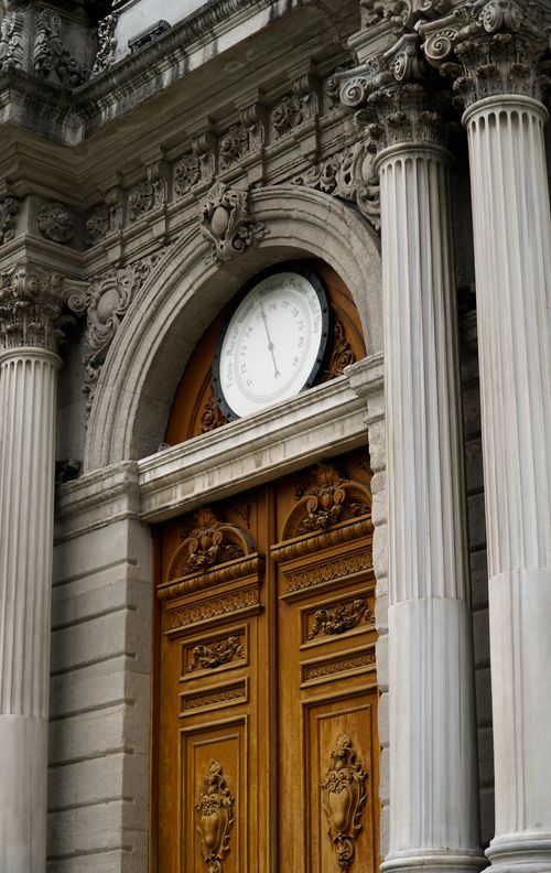 Free Intricate architecture featuring a clock above elegant wooden doors and decorative columns. Stock Photo